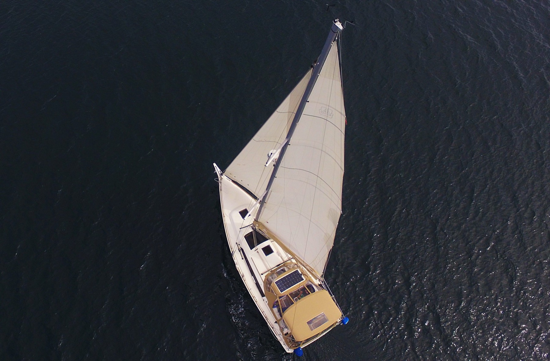 An aerial view of a sailboat cutting across dark water.